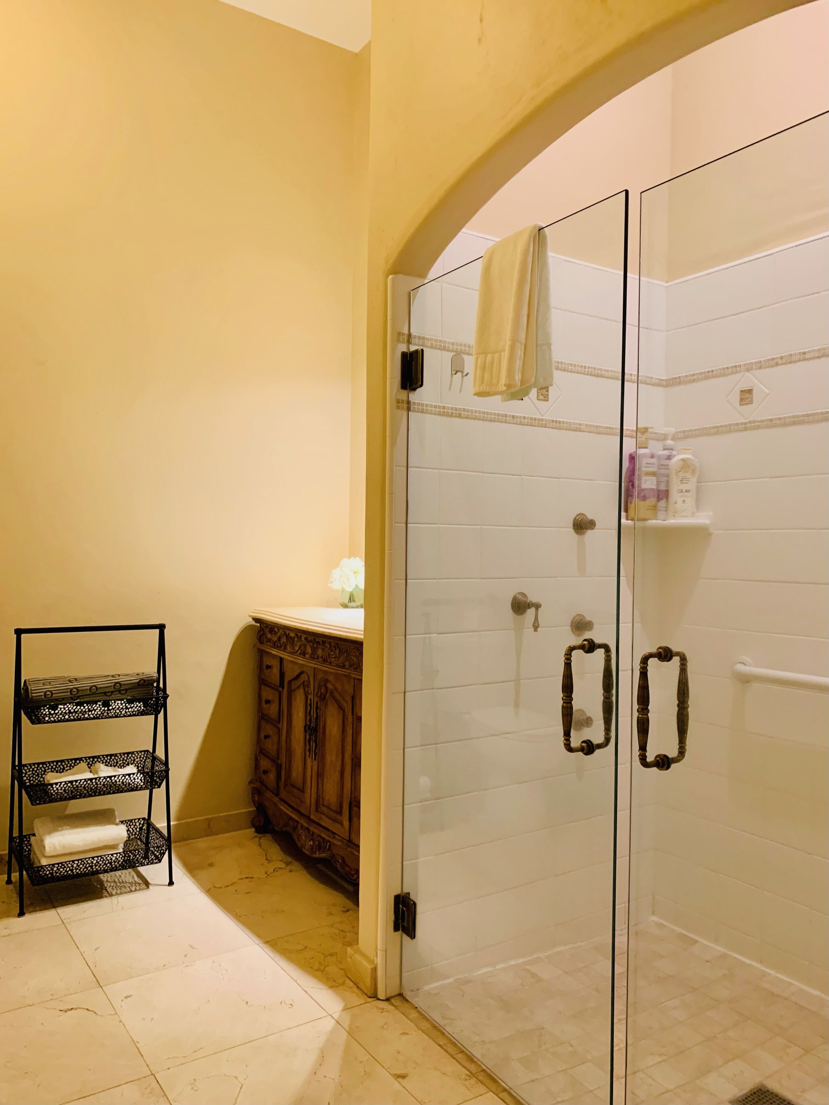 Une salle de bain avec une douche à parois de verre, un meuble en bois et une étagère en métal noir.