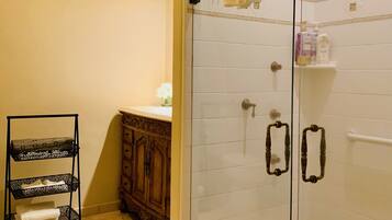 Une salle de bain avec une douche à parois de verre, un meuble en bois et une étagère en métal noir.