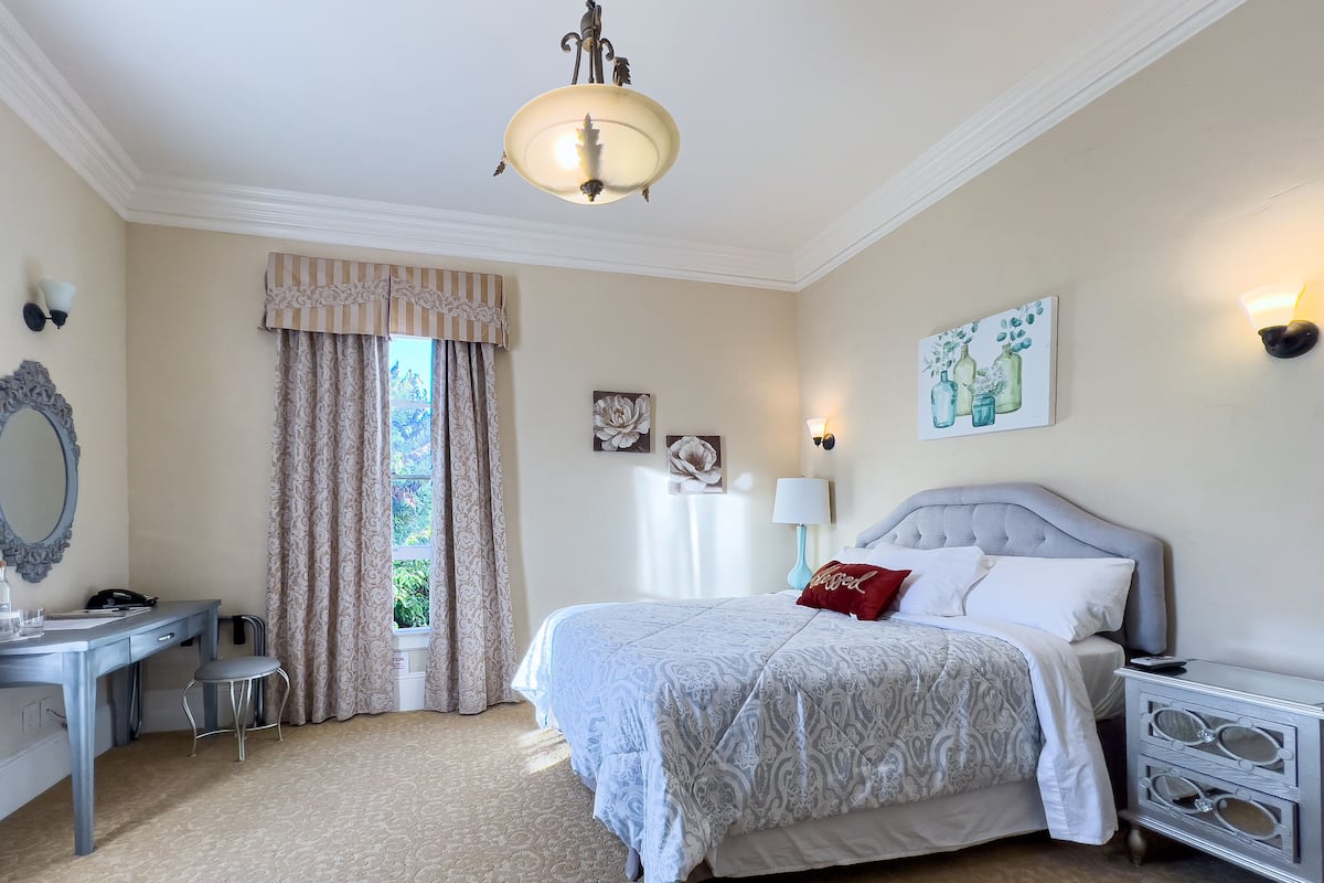 A bedroom with a bed, bedside tables, a desk, a chair, and a window with curtains.