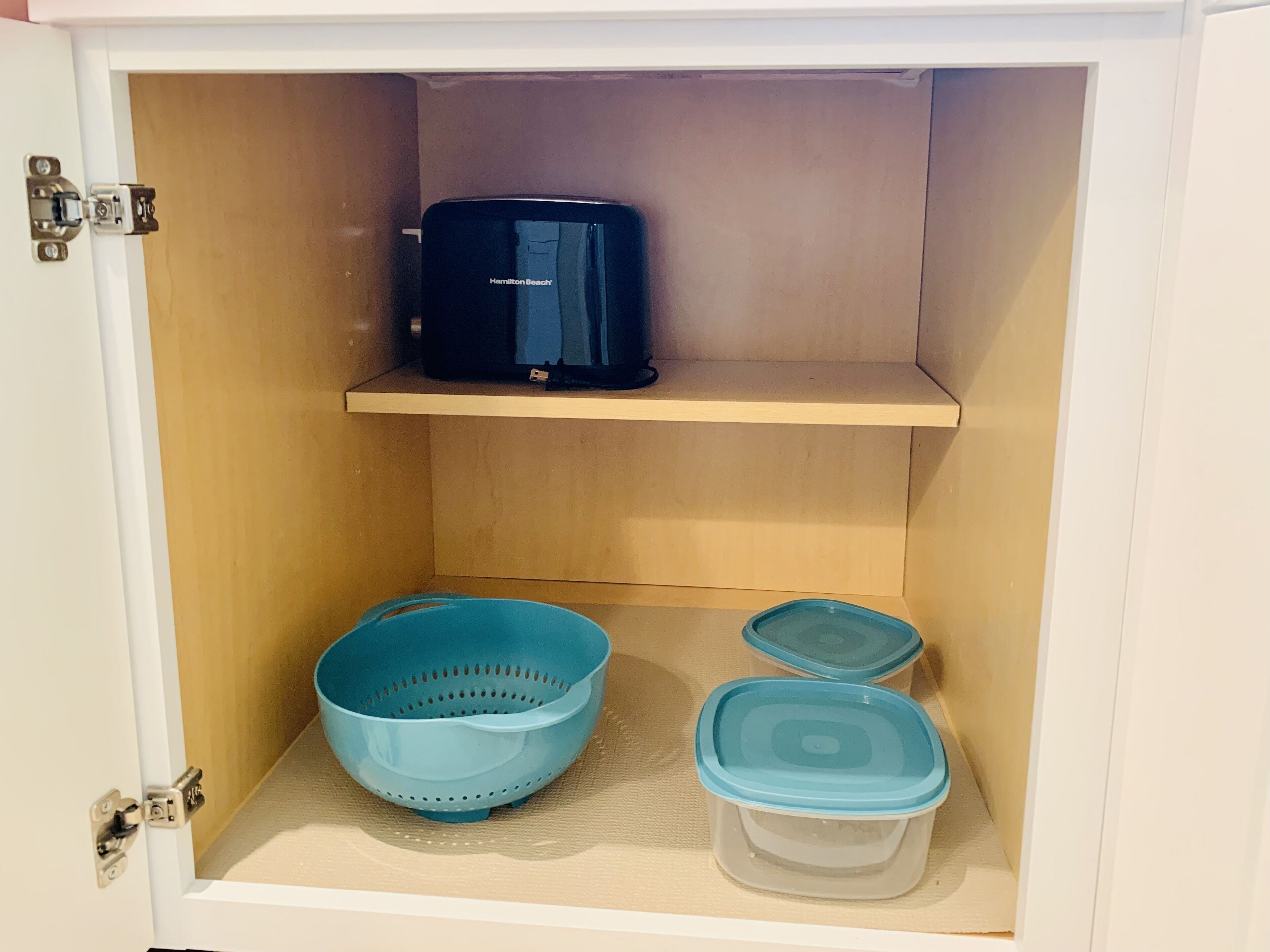 Ein Schrank mit einer Mikrowelle auf der oberen Ablage und zwei Behältern mit Deckeln auf der unteren Ablage.