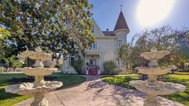 A two-story house with a prominent tower, a driveway, and two stone fountains. - Chateau Coralini (Salinas)