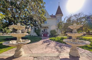 A two-story house with a prominent tower, a driveway, and two stone fountains. - Chateau Coralini (Salinas)