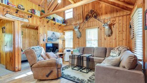 L’intérieur chaleureux d’un chalet avec des murs en bois, une cheminée, un canapé et une tête de cerf accrochée au mur.
