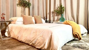 Een moderne slaapkamer met een groot bed, een nachtkastje, een lamp en een plant.
