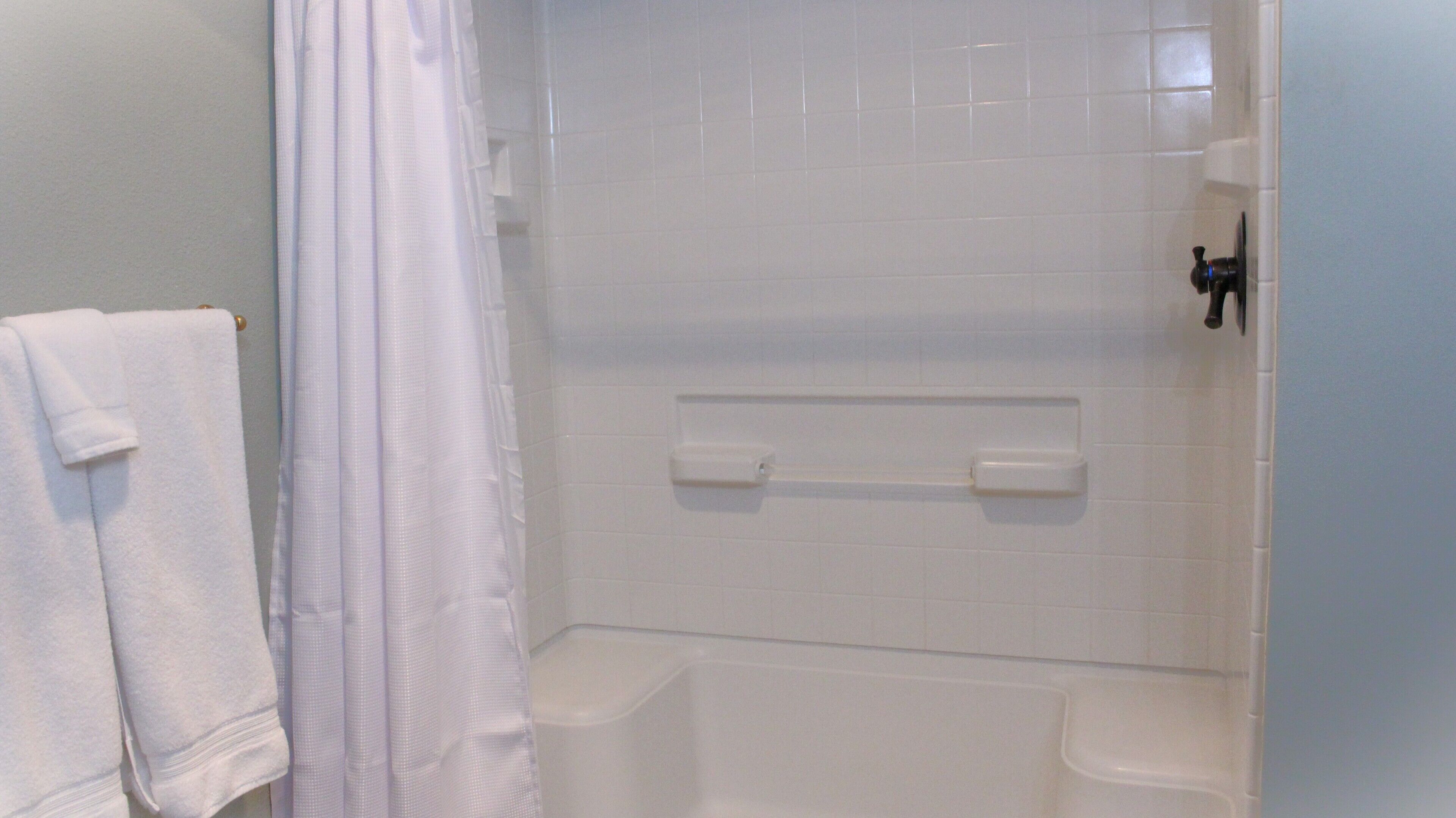 Un baño con azulejos blancos, una cortina de ducha y un perchero para toallas.