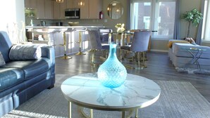 Een moderne woonkamer met een blauwe vaas op een marmeren tafel, een leren bank en een eethoek met barkrukken.