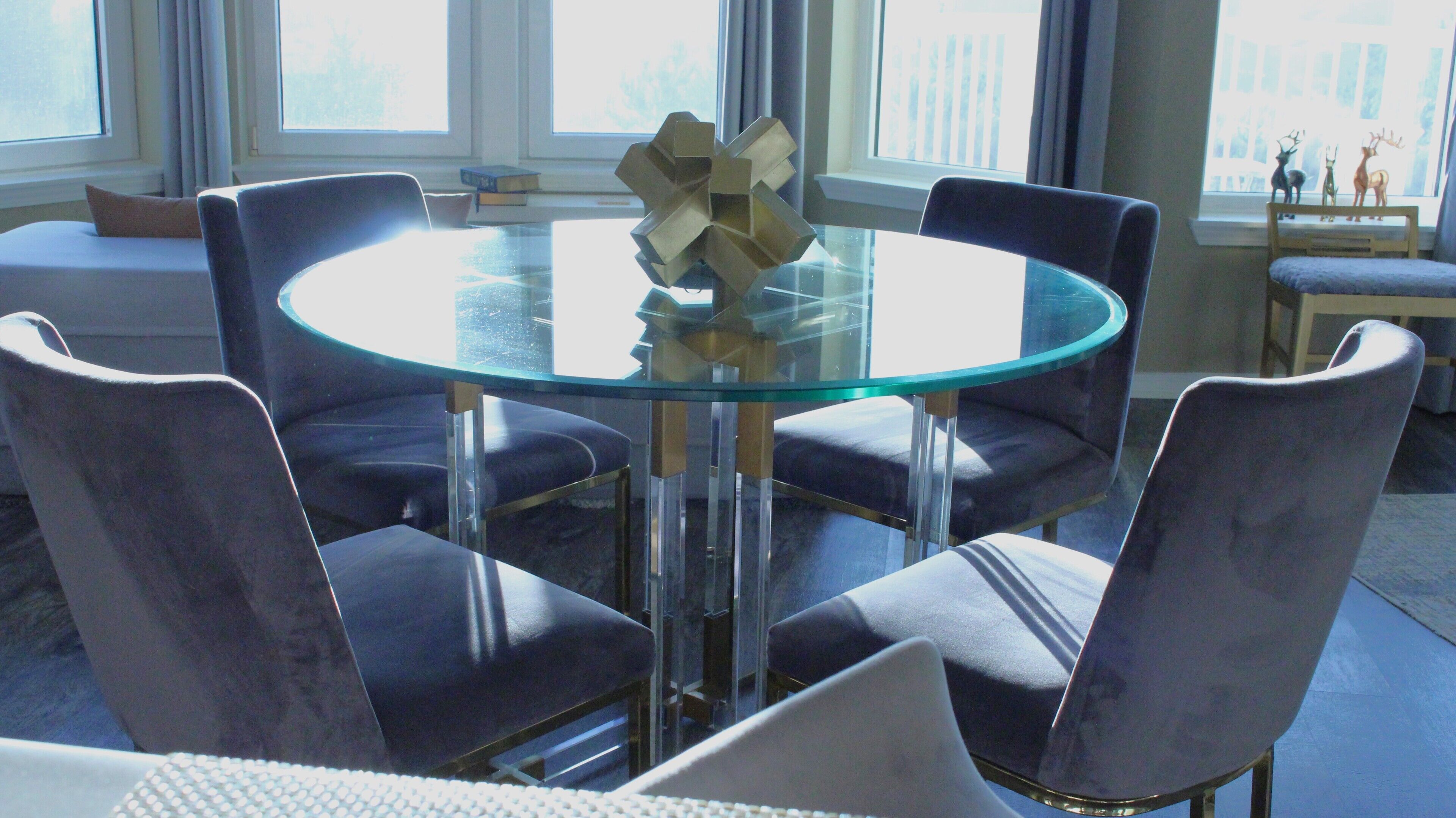 A modern dining area with a glass table surrounded by four chairs, a decorative metal sculpture, and a view of the city through large windows.