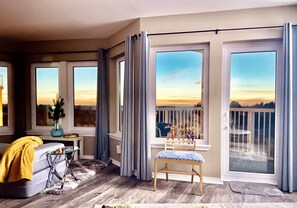 A spacious balcony with a view of the sunset, a comfortable seating area with a chair and a table, and a small table with a vase and books. - Stylish Oceanfront Escape 2 Master Suites King Bed (Long Beach)
