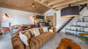 En moderne stue med træloft, et spiseområde med et træbord og stole, samt en trappe med sort gelænder.