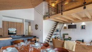 Et moderne køkken med træskabe, et spisebord dækket med tallerkener og glas, og en trappe til en etage ovenover.