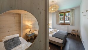 Et hyggeligt soveværelse med sengegavl i træ, et natbord med lampe, seng med gråt tæppe og et vindue med gardiner.
