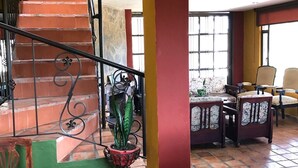 Una escalera con barandilla de metal, una planta en maceta y un comedor con sillas y una mesa.