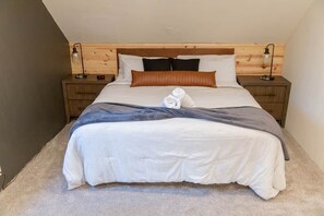 A neatly made bed with a wooden headboard, two bedside tables with lamps, and a carpeted floor.