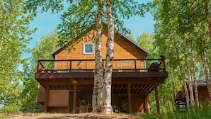 A wooden cabin with a balcony, surrounded by trees. - Luxury Lakefront Retreat | Sauna, Dock & Kayaks (Talkeetna)