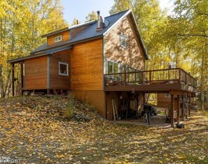 A wooden cabin with a balcony, surrounded by autumn leaves.
