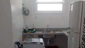 Eine kleine Küche mit Kühlschrank, Spüle und einem Fenster über der Arbeitsfläche.
