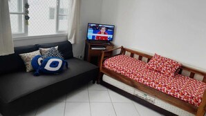 Ein kleiner Raum mit einer schwarzen Couch, einem hölzernen Bett mit einer rot-weißen Bettdecke und einem Fernseher auf einem Holztisch.