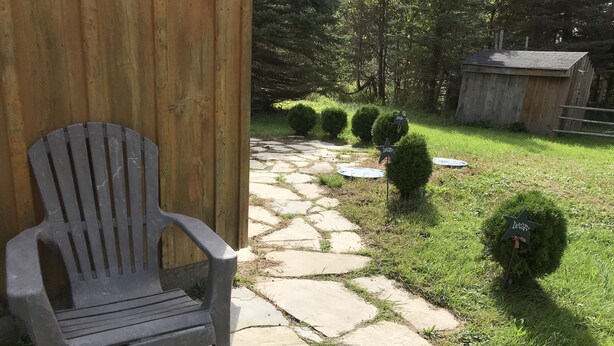 A stone pathway leading to a wooden building with a plastic chair outside. - Hepworth Studio Apartment, 3 Wooded Acres (Hepworth)