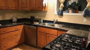 A kitchen with wooden cabinets, a stainless steel sink, a stove, and a dishwasher. - Hepworth Studio Apartment, 3 Wooded Acres (Hepworth)