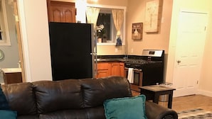 A living room with a brown leather sofa, teal cushions, a glass coffee table, and a kitchen in the background. - Hepworth Studio Apartment, 3 Wooded Acres (Hepworth)