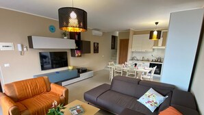 A modern living room with a sofa, armchair, and coffee table, a TV, and a kitchen in the background. - Palmito villa with pool in Baveno (Baveno)