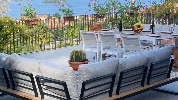 A terrace with a table set for dining, overlooking a coastal landscape with mountains and a lighthouse. - Palmito villa with pool in Baveno (Baveno)
