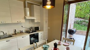 A modern kitchen with a dining area, a gas stove, a microwave, and a view of a garden through a glass door. - Palmito villa with pool in Baveno (Baveno)