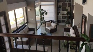 En rummelig opholdsstue med højt til loftet, store vinduer og en trappe op til et øvre plan.