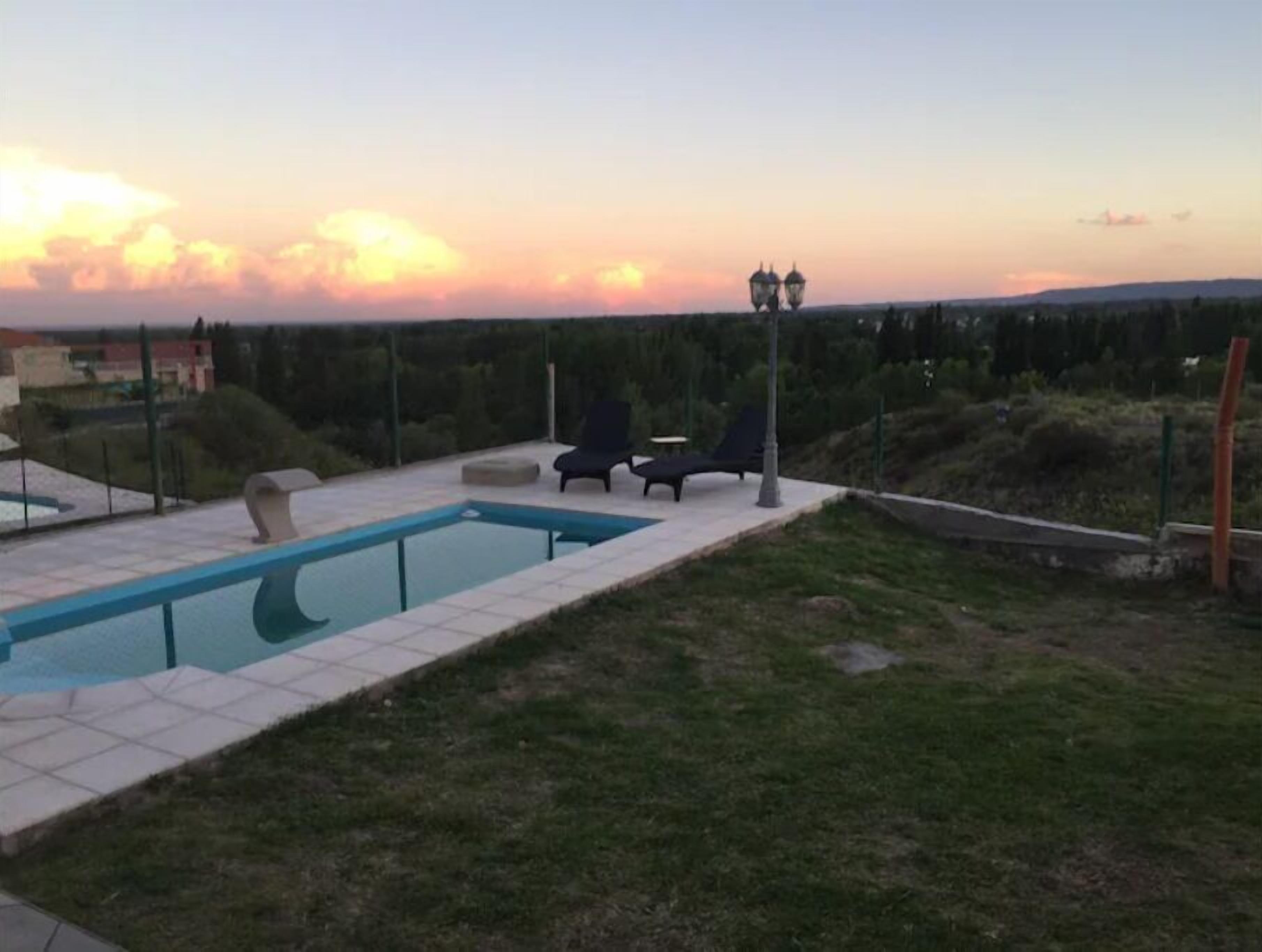 Ein rechteckiger Pool mit zwei Liegestühlen und einem Laternenpfahl, umgeben von einer Rasenfläche und einem Zaun.