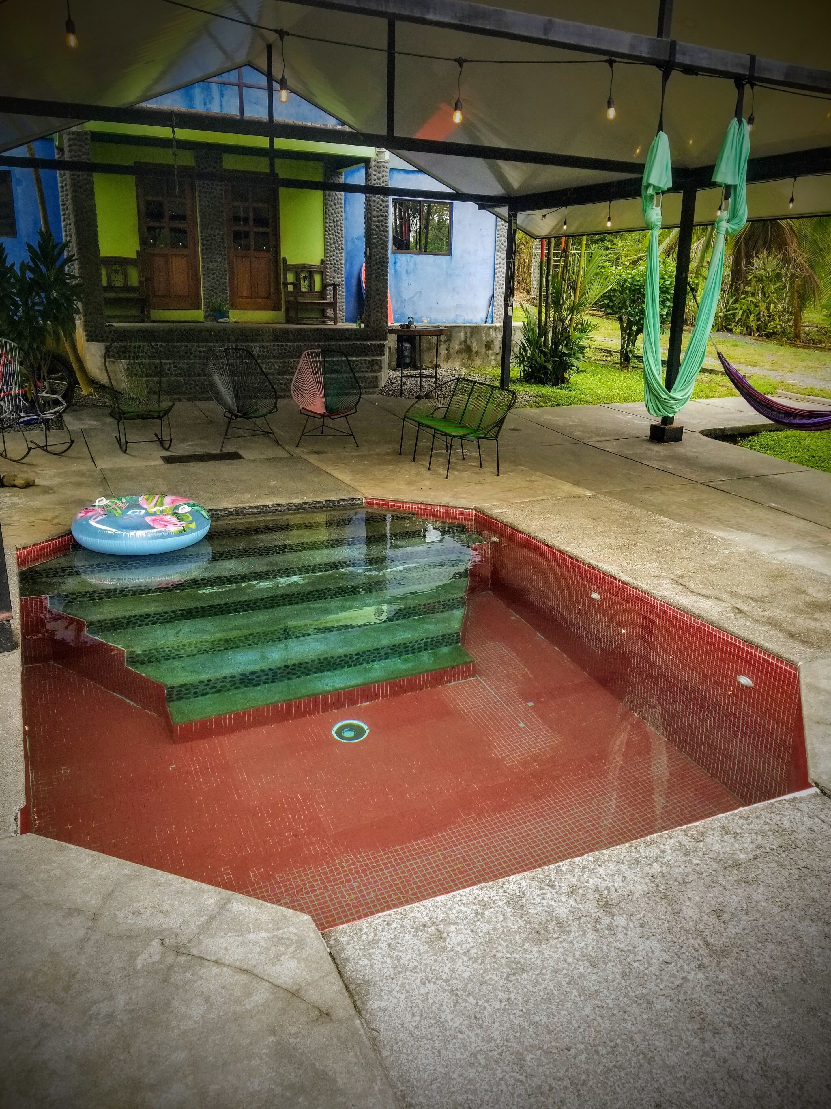 En pool med trappsteg som leder ner i vattnet, omgiven av utomhusmöbler och en hängmatta.
