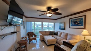 A living room with a ceiling fan, a flat-screen TV, a sofa, a small table, and a chair.