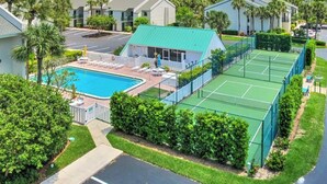 A residential complex with a swimming pool, tennis courts, and a covered patio area.