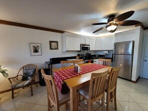 A compact kitchen with white cabinets, a stainless steel refrigerator, a microwave, and a ceiling fan. - OV 821 Tennis Court View - Paradise Vacation Rental in Ocean Village (Fort Pierce)