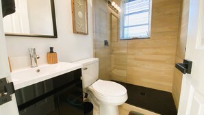 A modern bathroom with a white toilet, a black sink, and a glass shower enclosure. - POMPANO BEACH DELIGHT RETREAT 5' BEACH (Pompano Beach)