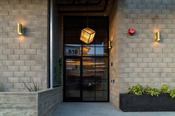 A building entrance with a glass door, a number "516" on the door, and two wall-mounted lights.