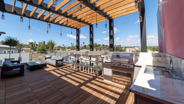 Une terrasse extérieure dotée d’une pergola en bois, de tabourets de bar, d’un barbecue et d’un évier.