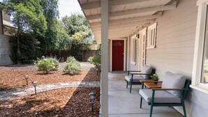 A covered porch with two green chairs and a small table, a red door, and a garden with mulch and small plants. - 1BR *HOUSE* in GLENDALE with PRIVATE FENCED YARD (p55) (Glendale)