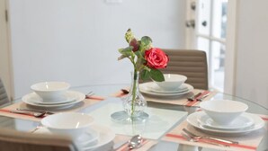 A round glass table with white plates, bowls, and cutlery. A clear vase with a red rose and green leaves is centered on the table. - 1BR *HOUSE* in GLENDALE with PRIVATE FENCED YARD (p55) (Glendale)