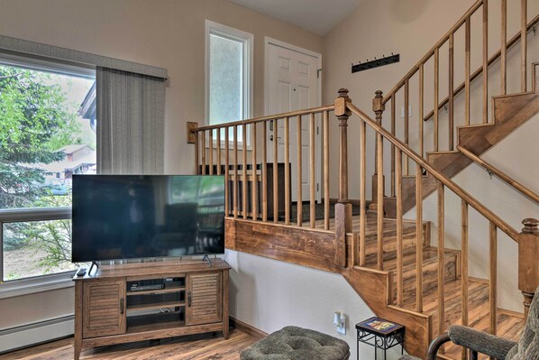 A living room with a wooden staircase, a TV on a wooden stand, and a window with curtains.