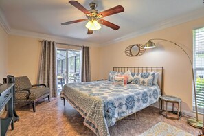 Ein Schlafzimmer mit Bett, Schreibtisch, Stuhl, Deckenventilator, Lampe und einem Fenster mit Jalousien.