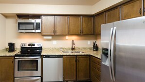 A kitchen with wooden cabinets, stainless steel appliances, a granite countertop, and a patterned rug.