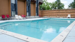 A rectangular swimming pool with clear blue water, surrounded by a wooden fence and several lounge chairs.