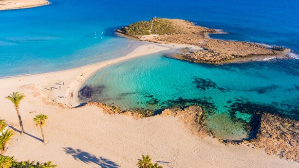 Een kuststrand met helder turquoise water, zandstranden en rotsachtige kliffen.