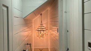 Un couloir aux murs recouverts de lambris blancs, agrémenté d’un lustre et d’un luminaire au plafond.