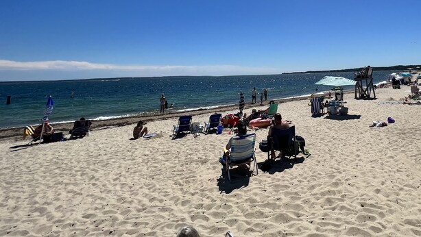 Une plage avec des personnes qui prennent des bains de soleil, des chaises de plage et des parasols.