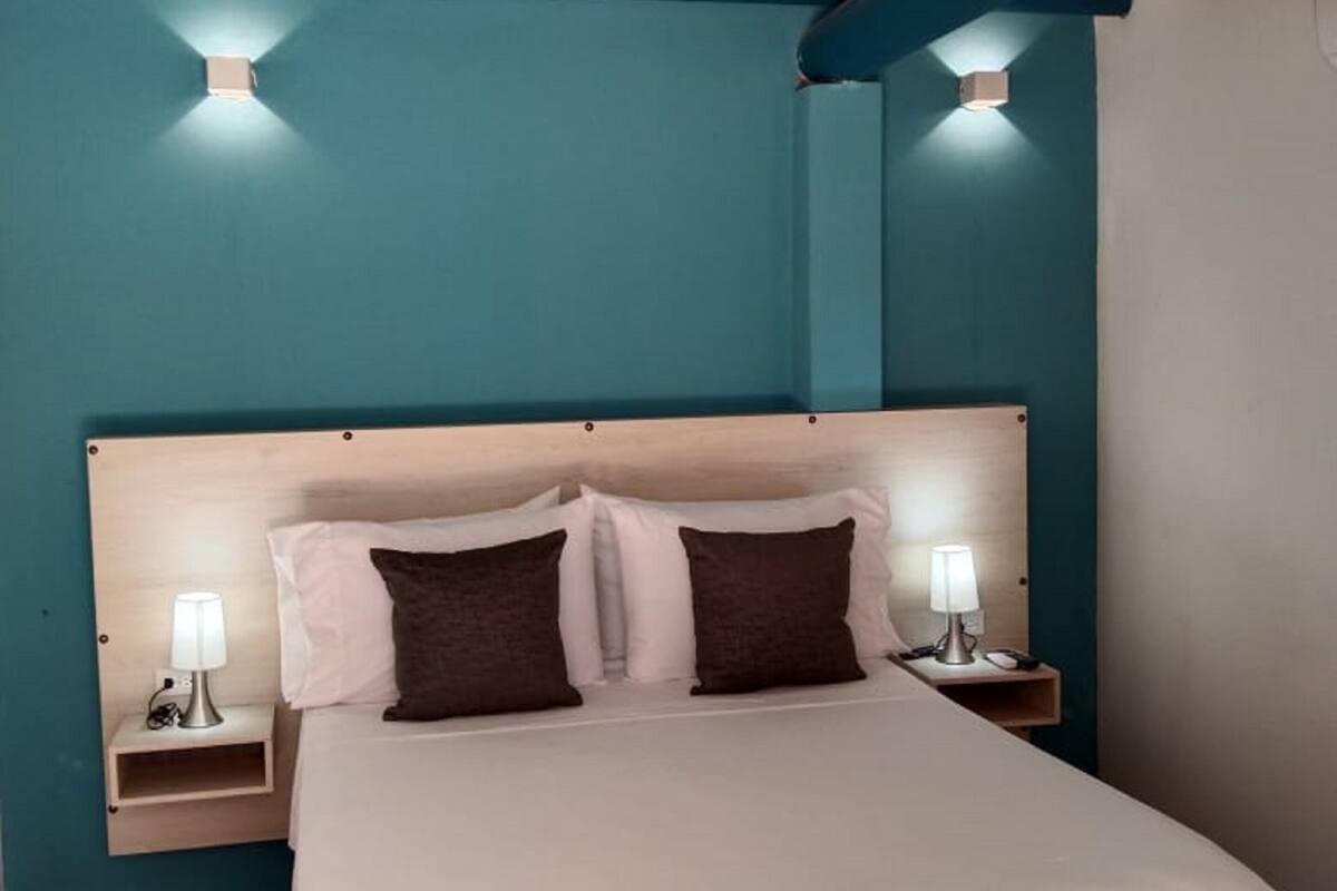 Une chambre à coucher avec un lit, deux tables de chevet et des lampes fixées au mur.