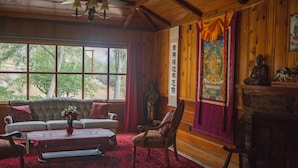 Una habitación acogedora con techo de madera, un sofá, una silla, una mesa con un florero y una ventana con cortinas.