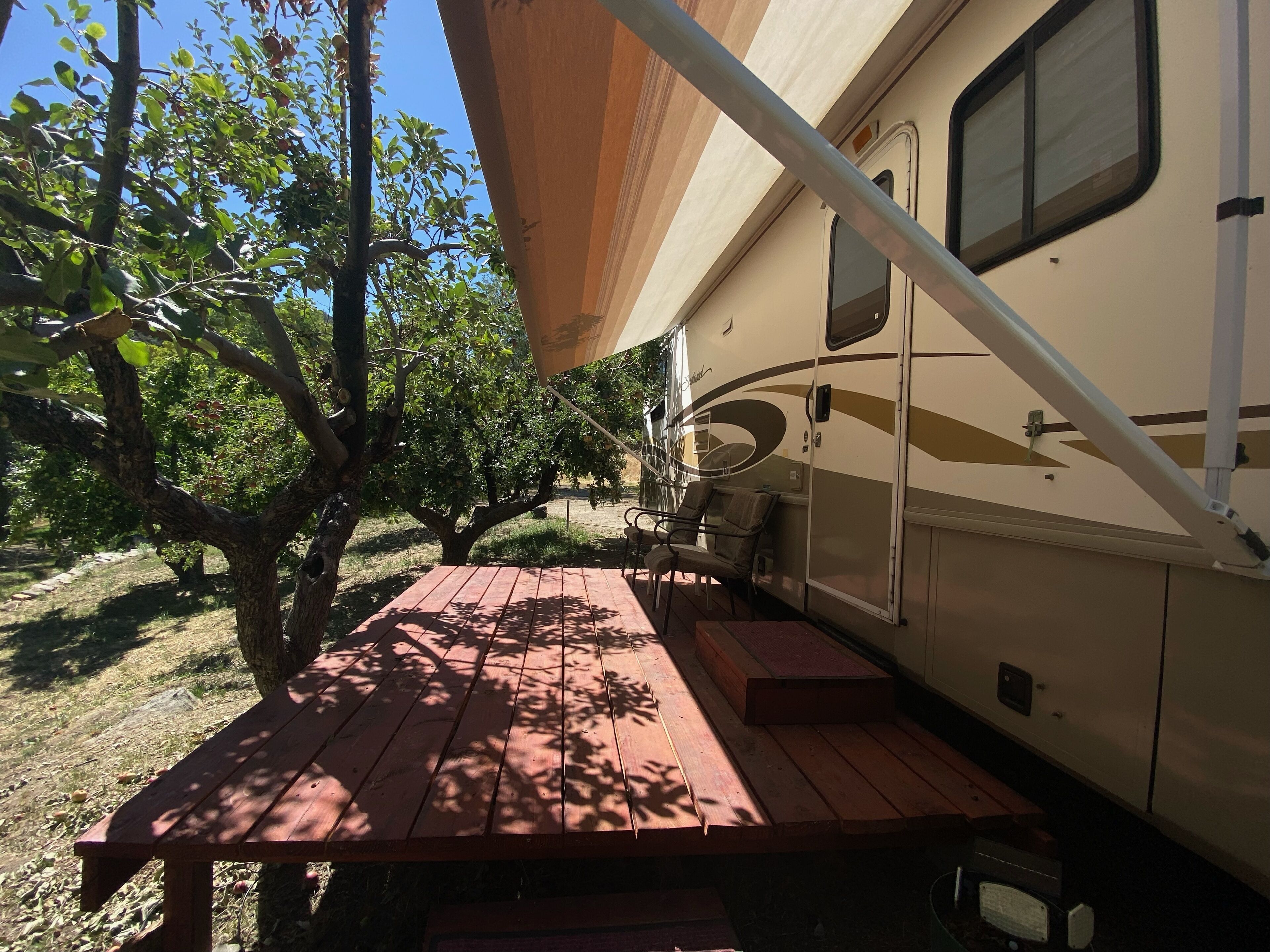 Een camper met een overdekte patio, een picknicktafel en een boom op de achtergrond.