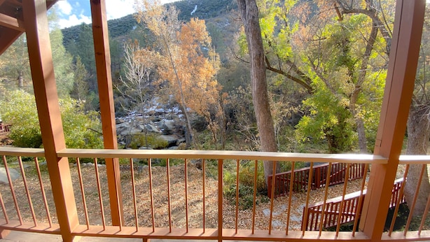 Una terraza de madera con barandilla metálica que da a un paisaje montañoso con follaje otoñal.