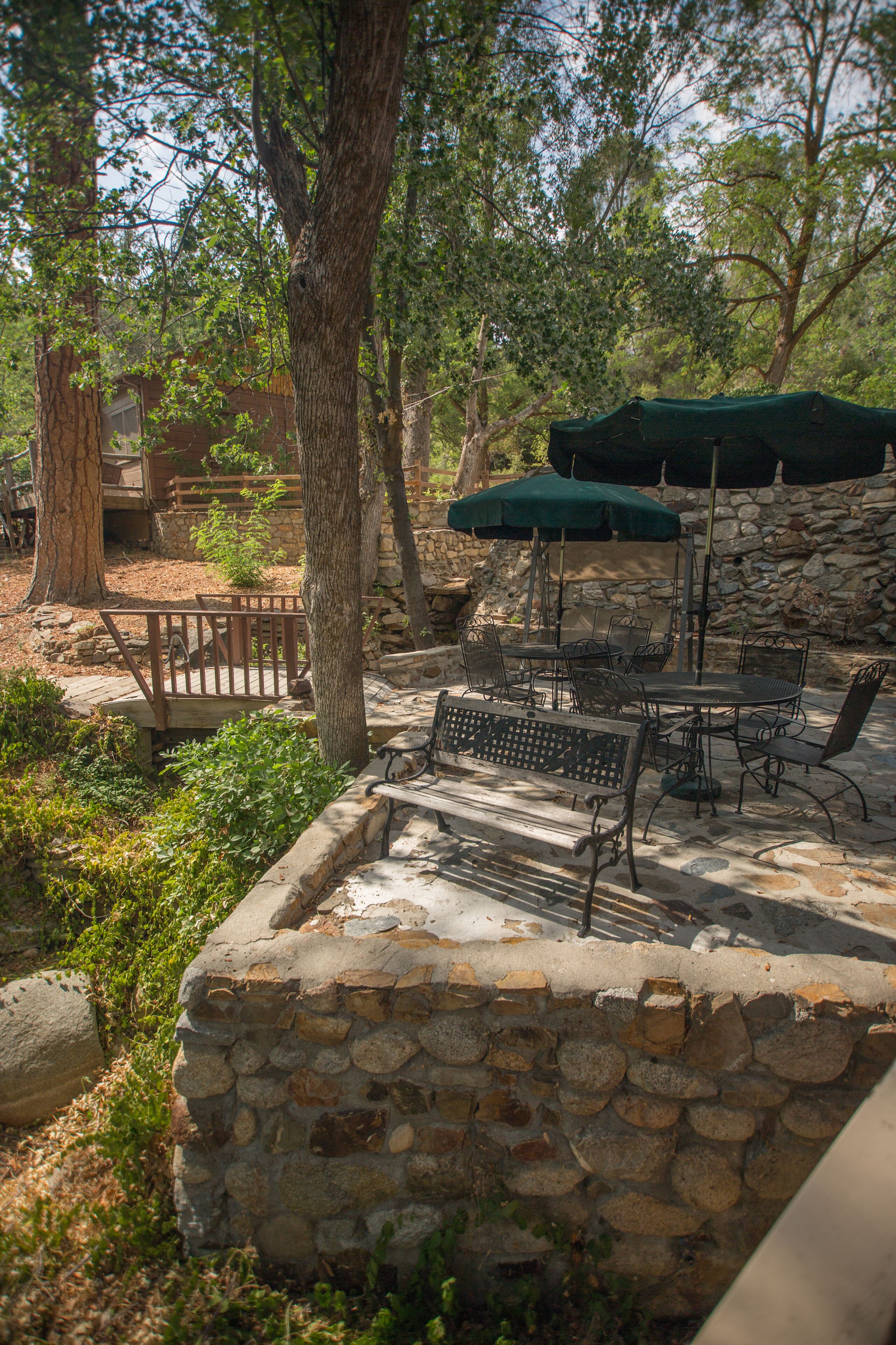 A stone patio with outdoor furniture, including a table and chairs, surrounded by trees.